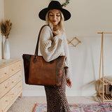 Woman holding a brown leather tote bag in a room with wooden furniture and decor.