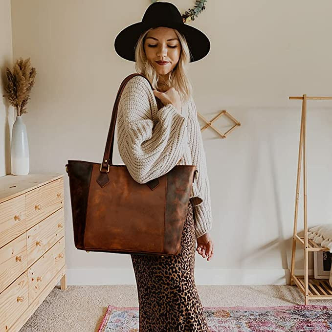 Woman holding a brown leather tote bag in a room with wooden furniture and decor.
